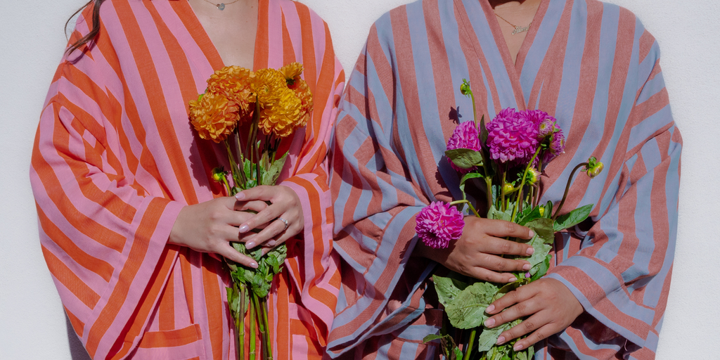 Image of two women in bathen robes, torso only, holding flowers. 